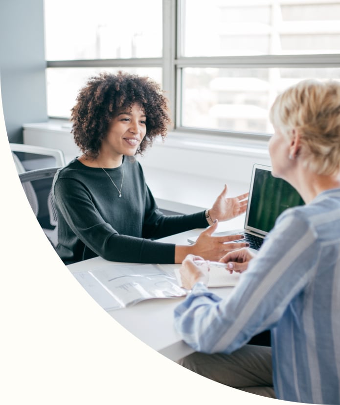 two businesswomen discussing loan options at desk over computer